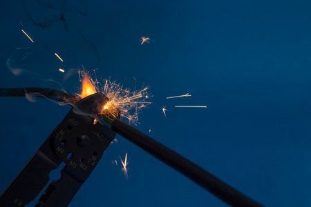 flame and sparks with wire stripper cutting  electrical cables, on dark blue color background , at...
