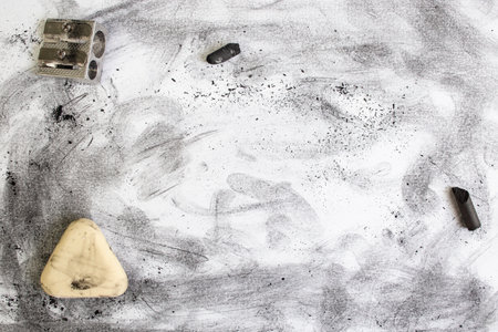 Black dust and smudges on white paper next to an eraser and a  sharpener