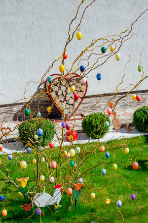 Colorful easter eggs hanging on tree branches in front of a  house yard