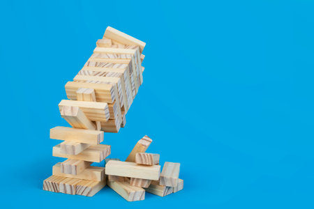 Collapsing wooden blocks tower on blue background, close up