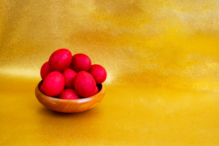 Red boiled easter eggs pile in a wooden bowl on golden glitter backgroundの写真素材