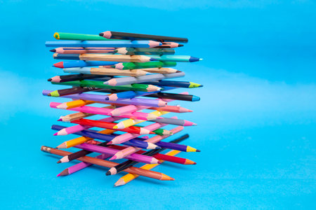 Stacked colored crayons stacked in the shape of a high tower illuminated  on blue