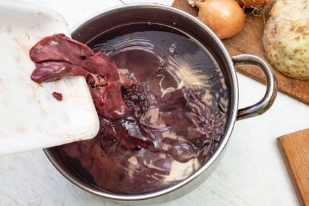 Pouring chicken liver in a cold water filled pot for washing before cooking, soft focus close upの写真素材