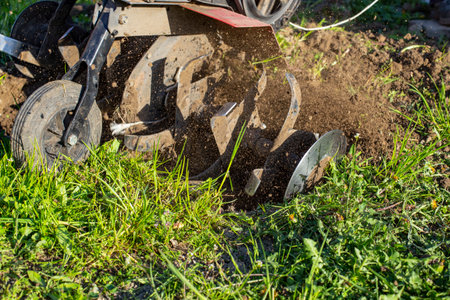 Garden tiller for cultivating field, loosens soil. Handheld motor plow throwing dirt with motion blurの写真素材