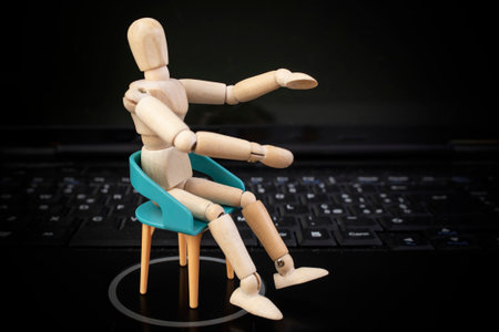 Wooden mannequin standing on chair on black laptop keyboardの写真素材