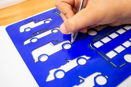 Child hand outlining and tracing a car shape with the help of a blue plastic stencil, soft focus close up, preschool leisure activityの写真素材
