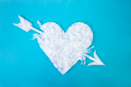 Cotton heart shape with an arrow thru, on blue background, abstract textured backdrop