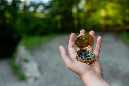 Male child hand holding a golden compass in the forest and pointing the way  at a crossroad, soft focus close upの写真素材