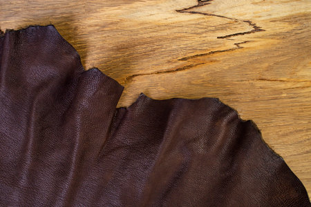 Dark brown ragged leather edge on oak wood texture, flat lay