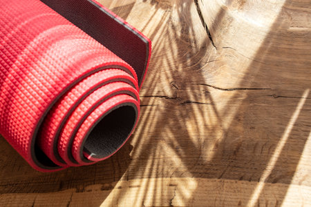 Rolled red yoga mat on hard wood flooring with palm tree leaves shadowsの写真素材