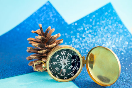 Golden compass and a pine cone on blue glitter defocused bokeh background, close up