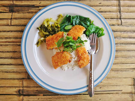 Steamed rice topped with fried crispy fish placed on a bamboo table