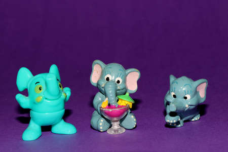 three little toy elephants on a purple background one elephant has a cocktailの写真素材
