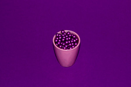 pink small cup glass full of purple beads on purple backgroundの写真素材