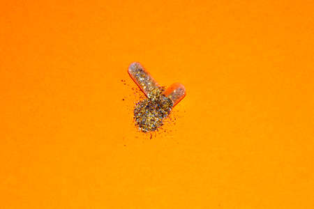an open pill from which golden glitter comes out on the orange background