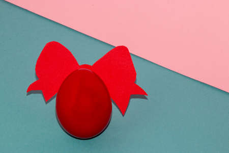 red egg with red bow on pastel blue pink background, copy space, creative art easter composition, beautiful designの写真素材