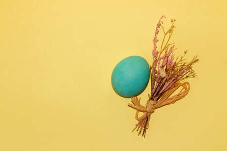 easter blue egg and a small bouquet on a pastel yellow background with lots of copy space, creative...
