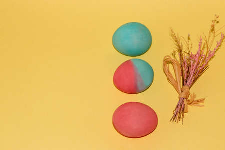 easter blue, pink and colorful egg lined up one below the other and a small bouquet on a pastel...