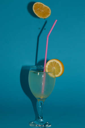 drink glass lemonade beautifully arranged and above it a lemon from which a few drops in a glass leak, creative art blue background, summer design, lemonade dayの写真素材
