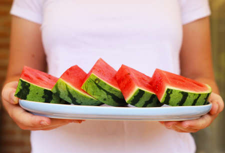 Woman's hands holding plate with pieces of watermelon.