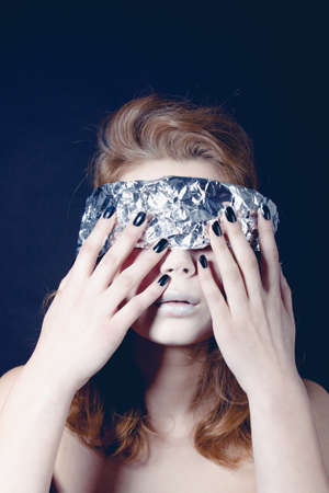 Portrait of pretty woman with close eyes, wrapped in foil looking forward standing on black background, horisontal pictureの写真素材