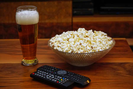 Pint of beer bowl of popcorn remote controllers and glasses on wooden background homemade entertainmentの写真素材
