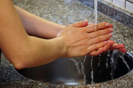 Woman washing hands with water and soap under the water in the kitchenの写真素材