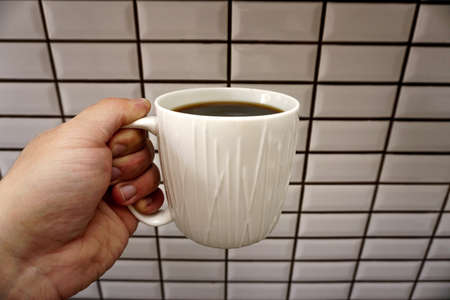 Man holding coffee mug in hand in the kitchen close up viewの写真素材
