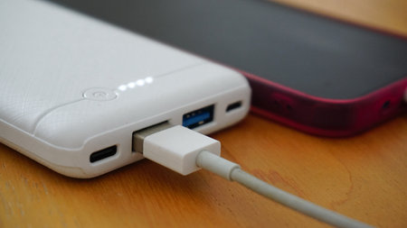 Smartphone being charged via powerbank on wooden table close up viewの写真素材
