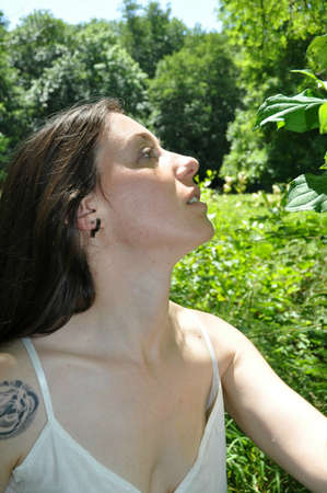 Beautiful young woman with the tattoo on the shoulder sniffing a leaf
