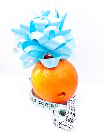 A ripe orange with a measuring tape and a blue gift decoration on top. Health concept.の写真素材