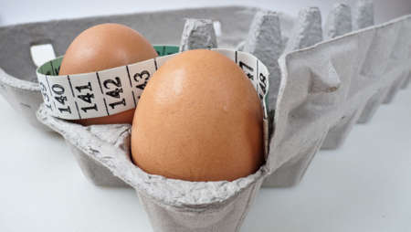 Two eggs in a grey carton with tape measure, selective focus. Health concept.の写真素材