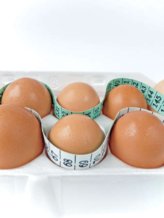 Several eggs in a white carton, surrounded by a measuring tape, selective focus. Health concept.の写真素材