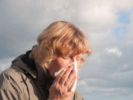 Mature woman sneezing into tissueの写真素材