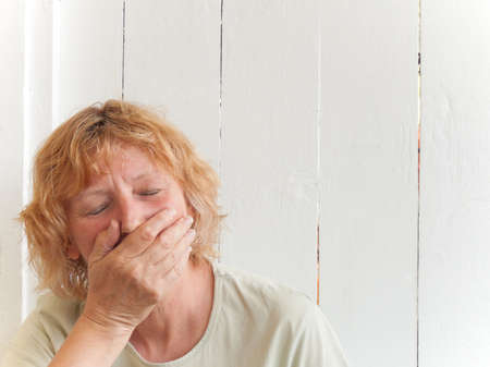 A mature woman against a white fence with hand over mouth.の写真素材