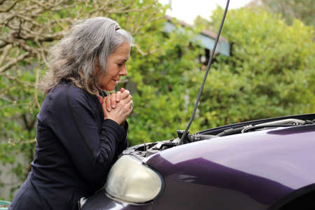 Mature woman praying over her car for safety and guidanceの写真素材