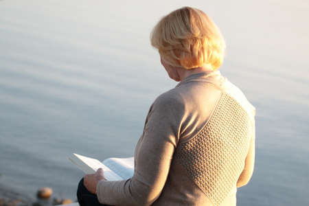 Senior adult woman reading book at the beachの写真素材