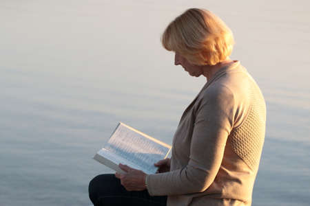 Senior adult woman reading Bible at the beachの写真素材