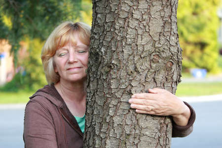 Mature woman with arm around tree trunk. Environmental concept.の写真素材