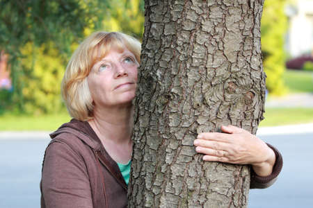 Mature woman arm around tree looking up. Mental healthpeaceenvironment concept.の写真素材