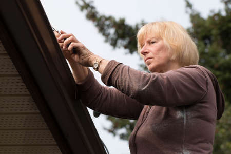 Mature woman cleaning out gutters on roof.の写真素材