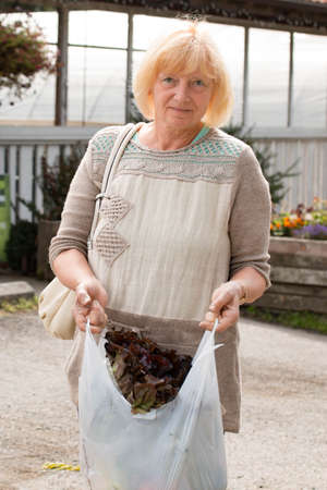 Mature woman shopping for produce locally; holding a bag of lettuce.の写真素材