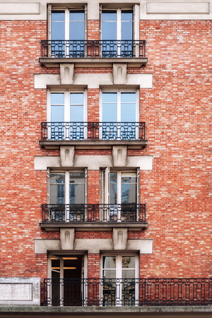Four pairs of windows with balconies from an openwork iron grating against a wall of red brick in the city of Paris.の写真素材