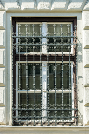 A window with a metal lattice and a wooden window frame with a cornice against a white wall.のeditorial素材