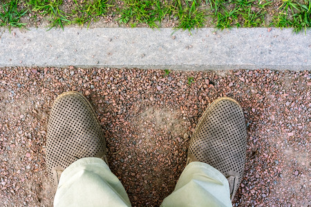 Fragment of legs in light beige trousers and brown shoes against the background of a footpath of small red stone with curb.の写真素材