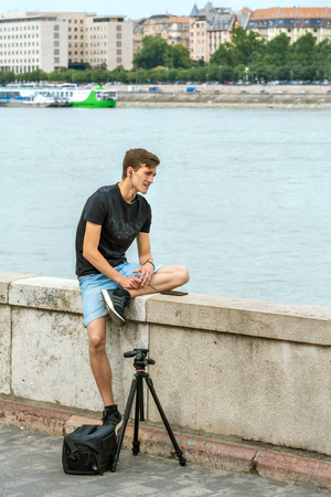 Budapest, Hungary, July 4: Young photographer talking on a mobile phone sitting on the parapet of the Danube embankment in Budapest, July 4, 2018.のeditorial素材