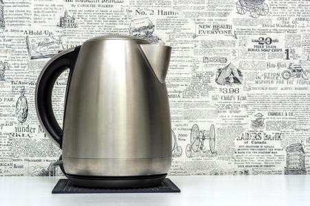 Image of a shiny metal electric kettle standing on a stand on a white table.