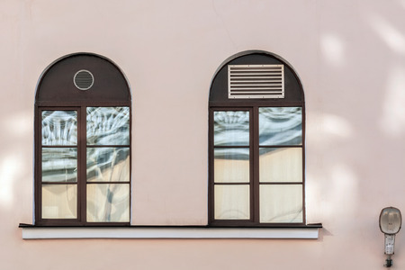 Two arched Windows with a dark brown frame against a pink wall. From the window series of St. Petersburg.の写真素材