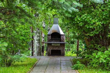 Brazier-oven for frying meat on the grid on the background of green bushes.の写真素材