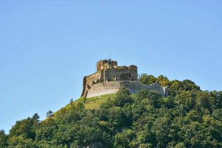 Kapusan castle ruins, on top of a forested mountain, with a flag on a tower against a clear blue sky in Slovakia, near the town of Presov.の写真素材